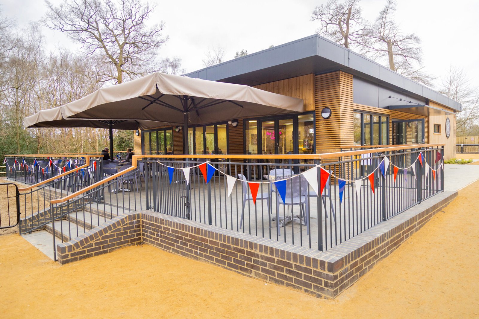 The completed Black Park Café, a net zero modular building by Modulek, featuring contemporary timber cladding and large glass windows, nestled in the woodland of Black Park.