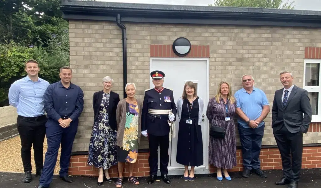 A group of nine people, including members of the Modulek team, school staff and Dorset Council officials, standing outside Cerne Abbas First School during a ribbon-cutting ceremony.