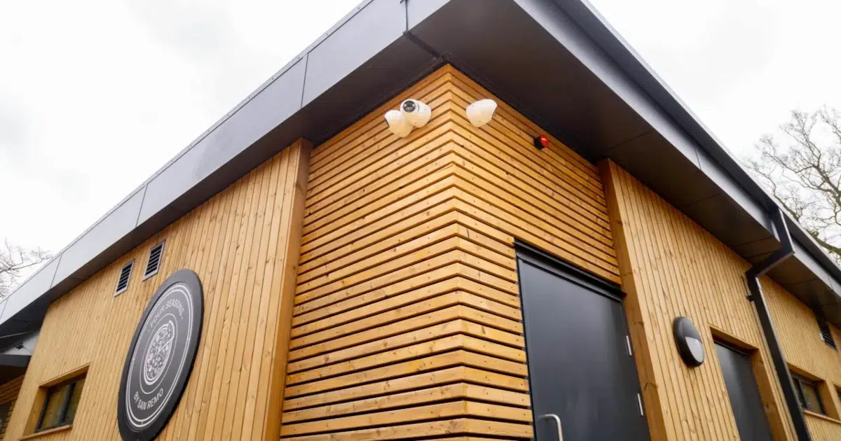 The exterior of the Black Park Café, a modern net-zero modular building with timber cladding, set amongst the trees of the country park.